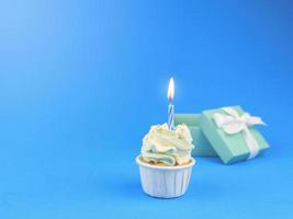 süßer kleiner kuchen mit bogenkerze und geschenkbox auf blauem hintergrund mit kopienraum. alles gute zum geburtstag party hintergrundkonzept. foto