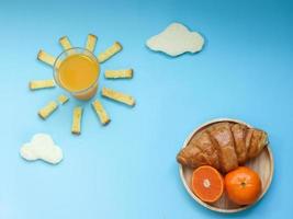 kreative frühstücksidee, sonnenaufgang morgens blauer himmel mit wolkenmahlzeit, orangensaft, knusprigem brot butterzucker, trübem weißbrot, croissant und orangenfrucht. Wachen Sie an einem helleren Tag mit Vitin C auf. foto