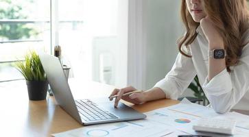 Porträt einer asiatischen jungen Frau, die im Büro am Laptop arbeitet foto