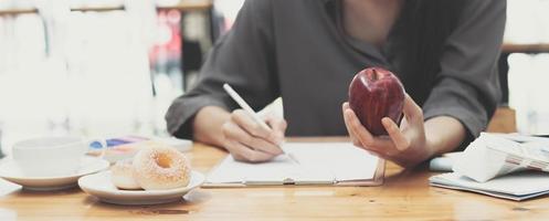 Attraktive junge asiatische Grafikdesignerin, die einen Apfel isst und ihr Design auf Papier an ihrem Schreibtisch skizziert. foto