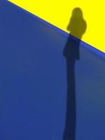 Defocus lange Beine Schatten einer stehenden Frau auf dem lebhaften blauen Bodenbelag und der gelben Wand, sommerlich hell mit Kopierraum, abstrakte Kunst foto