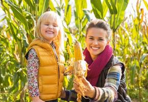 glückliche Mutter und Kind, die Mais zeigen, während in Maisfeld