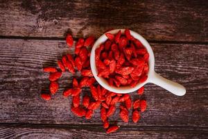 getrocknete chinesische Wolfsbeeren oder chinesisches Kraut der Goji-Beere oder Eherebe in der weißen Keramikschale isoliert auf Holzhintergrund. ausgewählten Fokus. foto