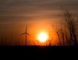 Silhouette Windkraftanlage auf Rasenfläche mit Dämmerung und Sonnenuntergang foto