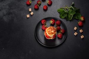 Quarkpfannkuchen mit geschnittenen Erdbeeren und Erdbeermarmelade auf einem Teller auf Betongrund foto