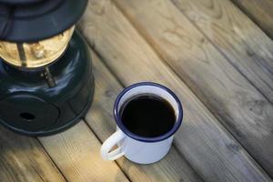 Selektiver Fokus weiße Emaille-Kaffeetasse und Kaffeeset im Garten mit alten Laternen in Campingatmosphäre. Weicher Fokus. foto