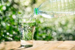 Gießen Sie Wasser aus einer Plastikflasche in ein Glas. der hintergrund der pflanzen im garten. Weicher Fokus. foto