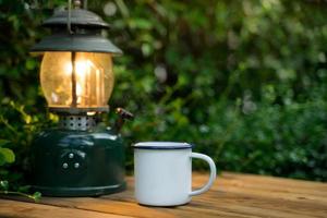 Selektiver Fokus weiße Emaille-Kaffeetasse und Kaffeeset im Garten mit alten Laternen in Campingatmosphäre. Weicher Fokus. foto