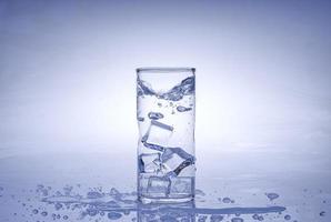 Eiswürfel fiel in das Wasserglas. Wasser spritzte aus dem klaren Glas. frisches Konzept foto