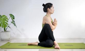 Frau, die Yoga auf der grünen Yogamatte macht, um zu Hause zu meditieren und zu trainieren. foto