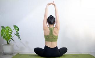 Frau, die Yoga auf der grünen Yogamatte macht, um zu Hause zu meditieren und zu trainieren. foto