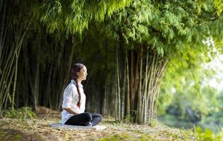 Frau, die entspannend Meditation im Bambuswald praktiziert, um Glück aus innerer Friedensweisheit für ein gesundes Geist- und Seelenkonzept zu erlangen foto