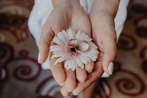 Brautaccessoires. Eheringe auf schöner Blume in den sanften Händen der Frau drinnen. horizontaler Schuss. urlaubs- und feierkonzept foto