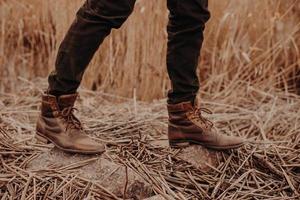 beschnittene aufnahme eines nicht erkennbaren mannes trägt alte lederbraune schuhe, posiert auf dem boden mit stoppeln, geht allein auf dem feld spazieren. foto