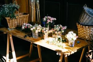 langer Holztisch mit verschiedenen Blumensträußen. angenehm riechende rosen, die in gläsern stehen. leere Holzkisten. Erstellung von Blumenstrauß. Rosen zur Dekoration arrangiert foto