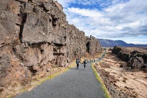 Touristen zu Fuß auf der Straße von Klippen gegen den blauen Himmel im Thingvellir-Nationalpark foto