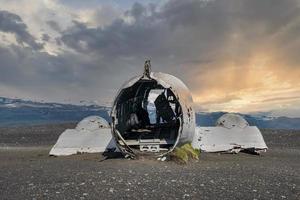 Verlassenes beschädigtes Flugzeug am schwarzen Sandstrand in Solheimasandur bei Sonnenuntergang foto