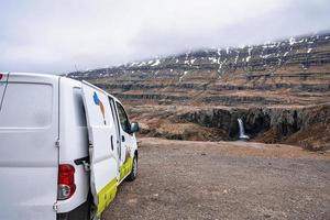 Van auf einer Klippe mit Blick auf den Folaldafoss-Wasserfall gegen den felsigen Berg geparkt foto