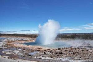 malerischer blick auf den strokkur-geysir, der inmitten der landschaft gegen den blauen himmel ausbricht foto