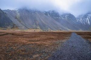 weg, der zu schneebedeckten bergen führt, die im nebel gegen den himmel bedeckt sind foto