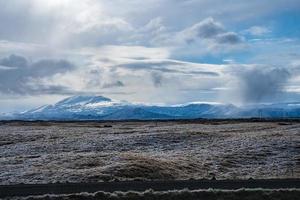 Blick auf die Straße durch grasbewachsene Landschaft und schneebedeckte Berge gegen bewölkten Himmel foto