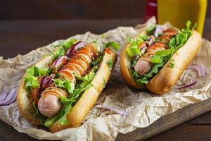 Hausgemachter Hot Dog mit Wurst, Salat, Karotten, Gurken und Tomaten auf Holzhintergrund foto