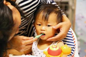 Porträt der Mutter, die dem süßen Baby beibringt, wie man die Zähne mit der Zahnbürste putzt. asiatischer junge mit mutter. foto