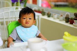 beleidigter kleiner asiatischer junge während des frühstücks. Baby unglückliches Gesicht. foto