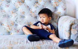 Frecher asiatischer Junge sitzt auf hellblauem Sofa im Wohnzimmer. foto