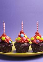 helle Süßigkeiten bedeckte Cupcakes vor einem lila Hintergrund foto