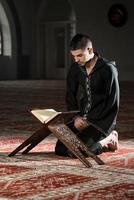 Der muslimische Mann in Dishdasha liest den Koran foto