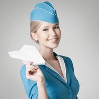 charmante Stewardess hält Papierflugzeug in der Hand. grauer Hintergrund
