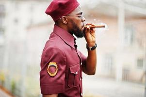 Porträt eines afroamerikanischen Militärs in roter Uniform, Sonnenbrille und Baskenmütze. Kapitän Zigarre rauchen. foto