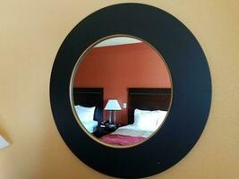 Schwarzer runder Hotelspiegel an der Wand mit Bett und Lampe foto