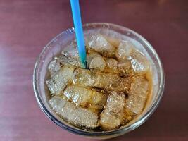 Soda und Eis in einem Glas mit einem blauen Strohhalm auf dem Tisch foto