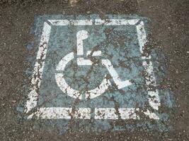 Abgenutztes blaues Rollstuhl- oder Handicap-Schild auf Asphalt foto