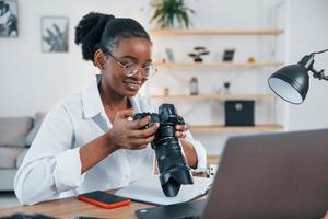 am Tisch sitzen. junge afroamerikanische frau im weißen hemd ist zu hause foto