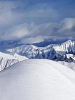 Spitze eines schneebedeckten Abhangs abseits der Piste und bewölkter Berge