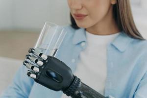 Hochtechnologie-Roboterarmprothese. Behindertes europäisches Mädchen hält ein Glas Wasser. foto