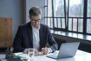 Fokussierter männlicher Banker schreibt Notizen auf Haftnotizen, während er von zu Hause aus arbeitet foto