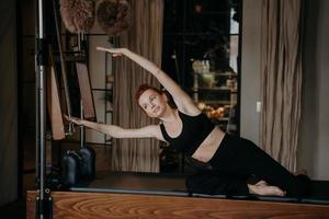 junge weibliche pilates-lehrerin, die auf cadillac reformer trainiert und dehnt foto