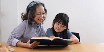 glückliche asiatische Familiengroßmutter, die zu Hause dem Kinderbuch der Enkelin vorliest foto