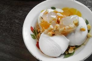Kokosnuss-Eiscreme nach thailändischer Art mit gerösteten Erdnüssen, süßer Ananas und süßen Palmkernen, serviert auf Vintage-Emailgeschirr foto