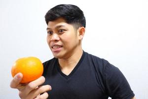 attraktiver asiatischer Mann, der Orangen isst. isoliert auf weißem Hintergrund foto