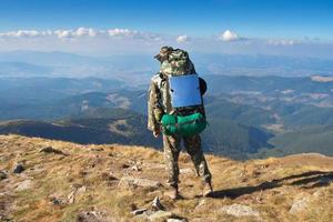 männlicher Wanderer steht auf einem Berggipfel foto