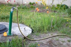 Sanitär, Wasserpumpe aus einem Brunnen. ein Außenwasserhahn mit einem daran befestigten gelben Gartenschlauch. Bewässerungswasserpumpsystem für die Landwirtschaft. Schlauch im Garten zum Gießen, sonniger Sommertag. foto