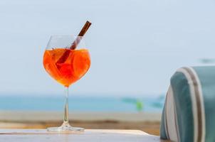 Ein Glas Orangencocktail wird mit verschwommenem Meereshintergrund für Urlaubs- und Sommergetränkekonzept auf den Tisch gestellt. foto