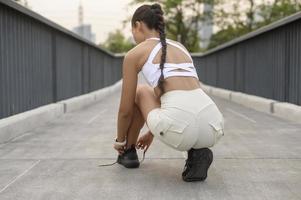 junge fitnessfrau in sportbekleidung, die schnürsenkel im stadtpark bindet, gesund und lebensstil. foto