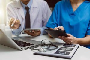 Hand des Medizinarztes, der mit modernem Computer und Smartphone arbeitet, digitales Tablet mit seinem Team auf weißem Schreibtisch als medizinisches Konzept im Morgenlicht foto
