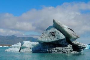 Heller klarer blauer und schwarzer Eisberg, der im blauen kalten Wasser des Jokulsarlon-Sees in Island 1 schwimmt foto